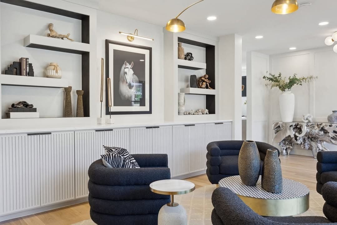 The sitting room at 13739 Hughes Lane, fluted white cabinetry along one wall with black lined niches above it and navy bouclé chairs under a brass arc lamp.
