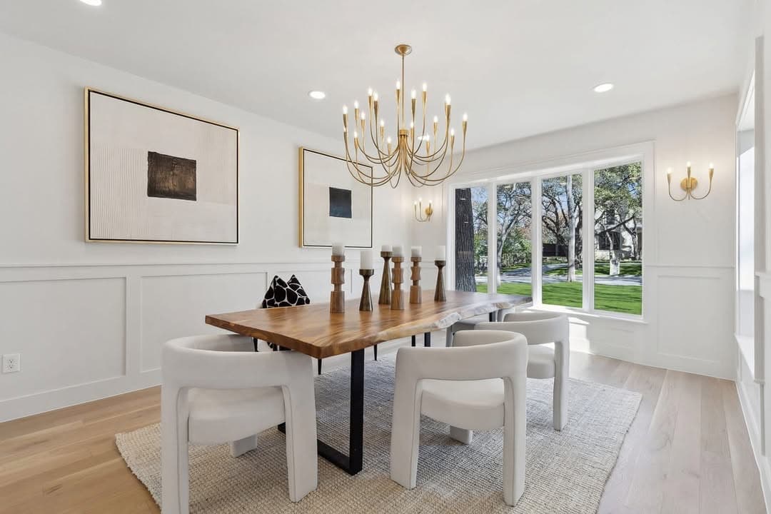 The dining room at 13739 Hughes Lane, a live edge walnut table under a brass chandelier with panelled wainscot and a bay window onto the front lawn.
