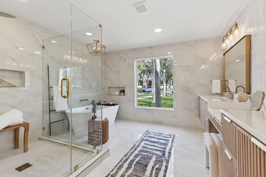 The primary bath at 13739 Hughes Lane, a freestanding tub under a window beside a glazed shower, the walls run in marble the full height.