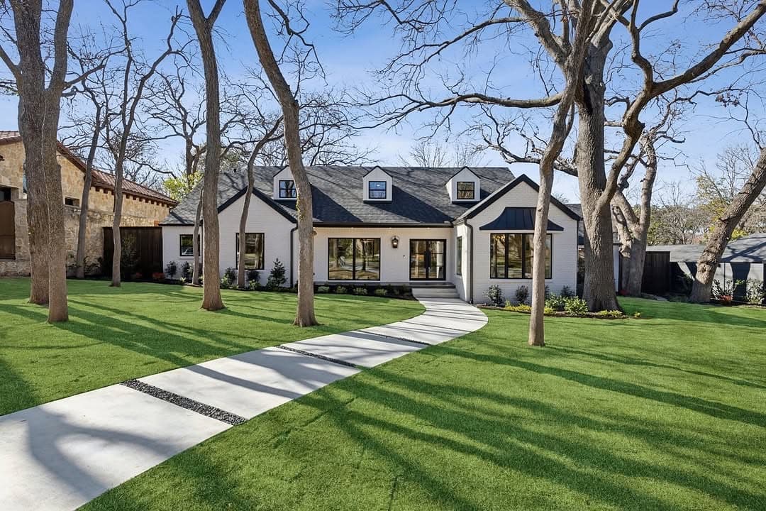 The front of 13739 Hughes Lane, a white brick house with dormers under a dark roof, a paved walk crossing the lawn between bare oaks.