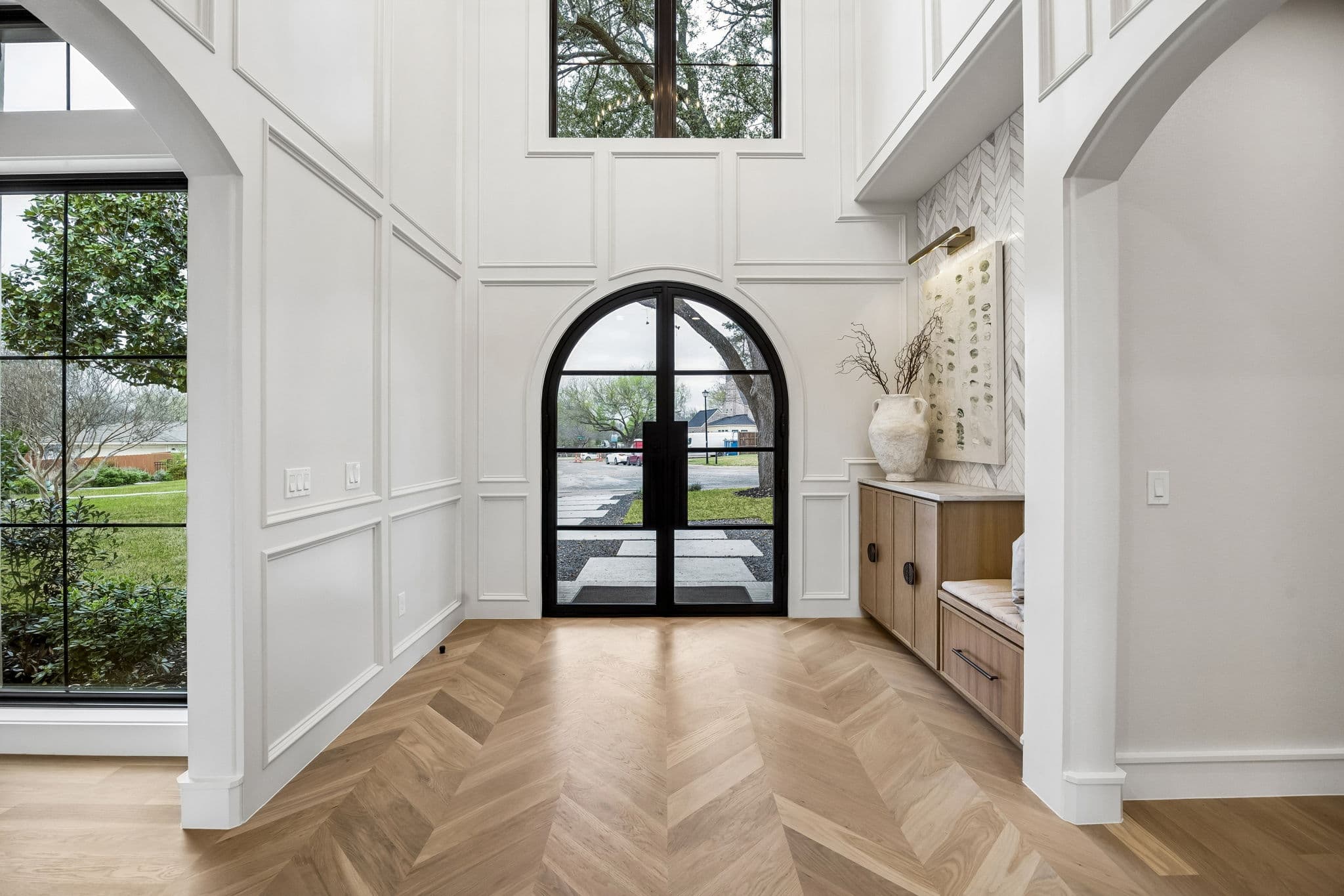 The entry hall at 7272 Tangleglen, double height with an arched steel door at the end of it and herringbone oak running the length of the floor.