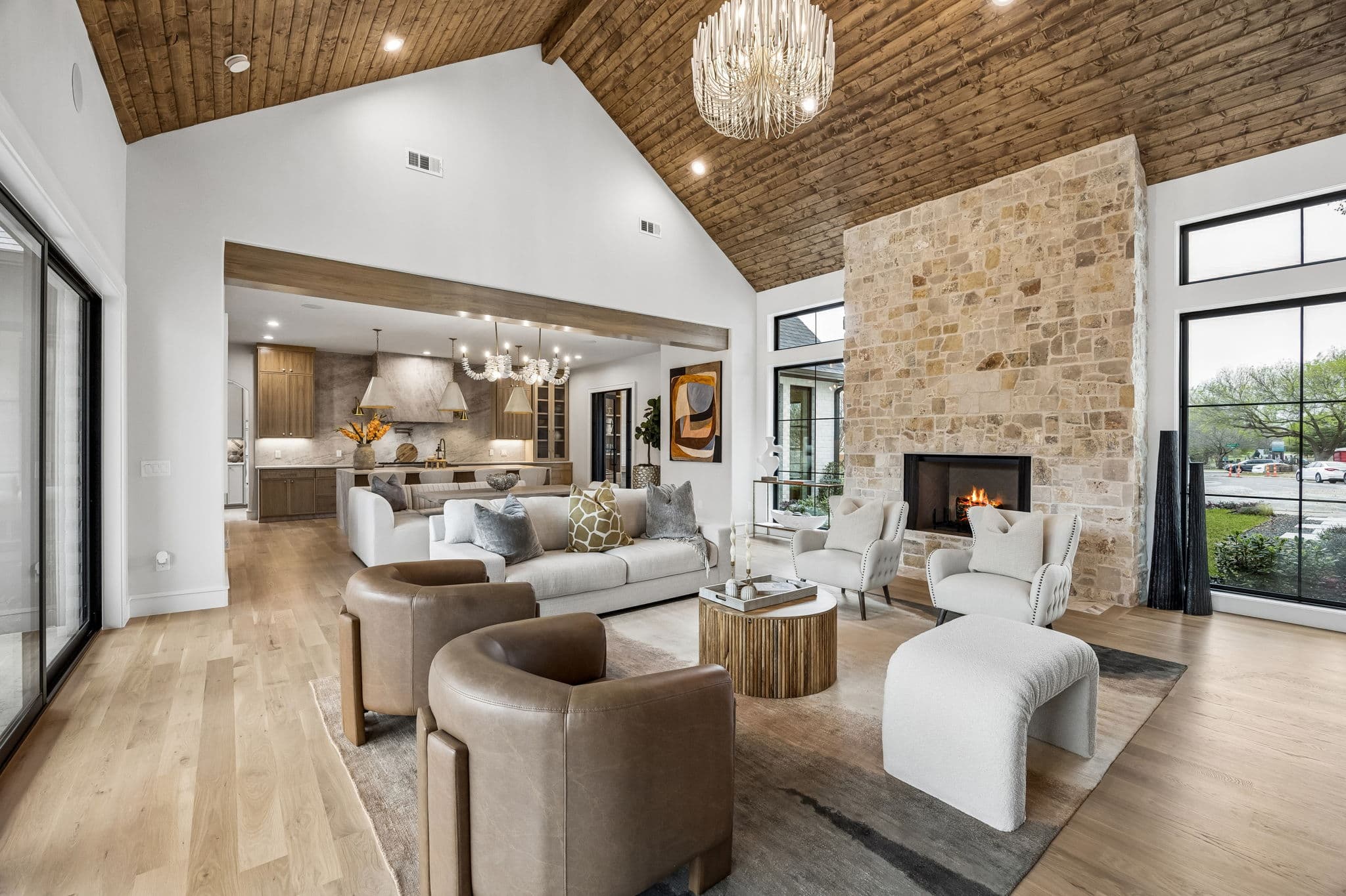 The great room at 7272 Tangleglen, a vaulted ceiling clad in wood over the seating, opening to the kitchen at the far end.