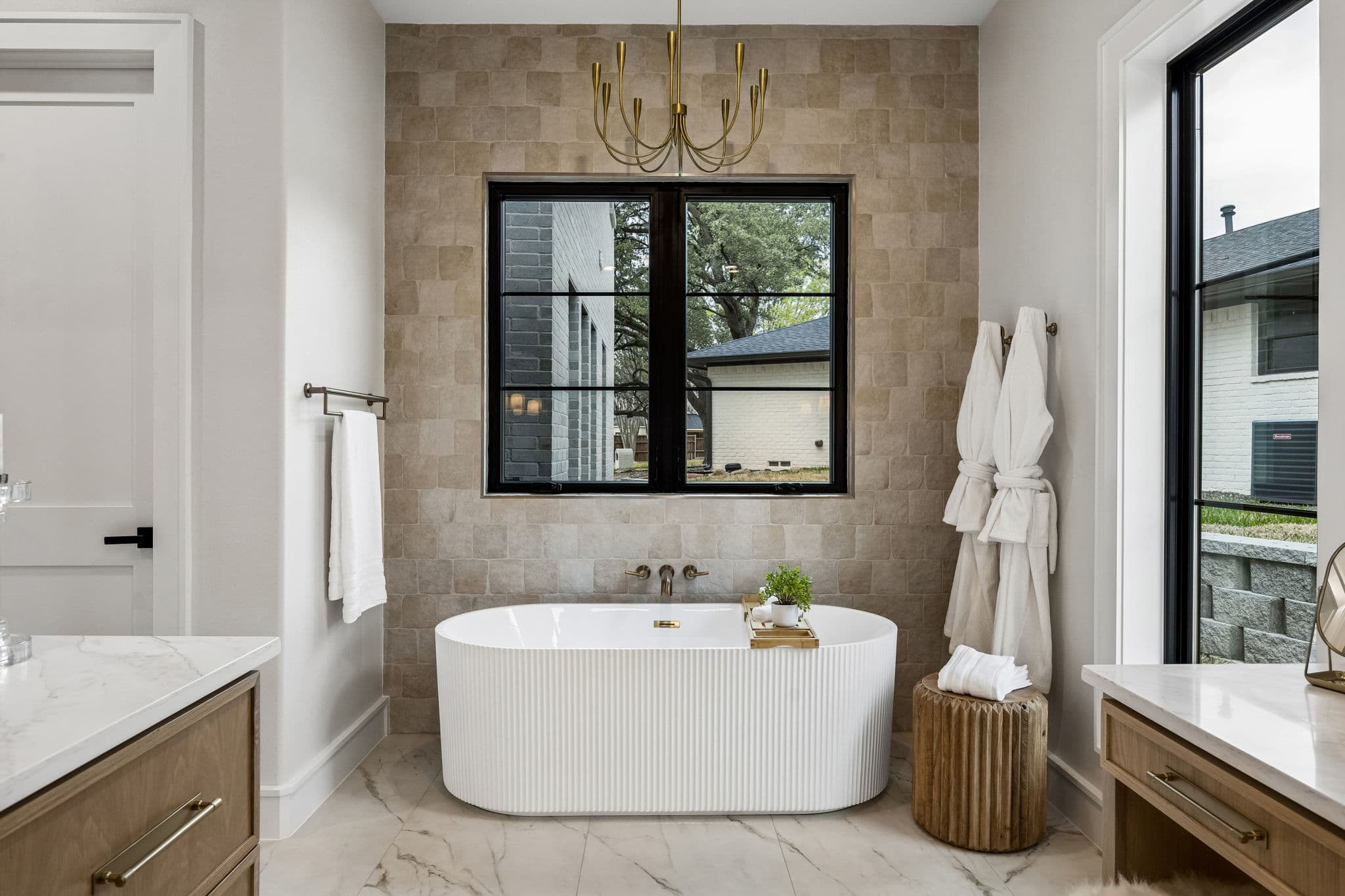The primary bath at 7272 Tangleglen, a fluted freestanding tub under a black steel window on stone tile.