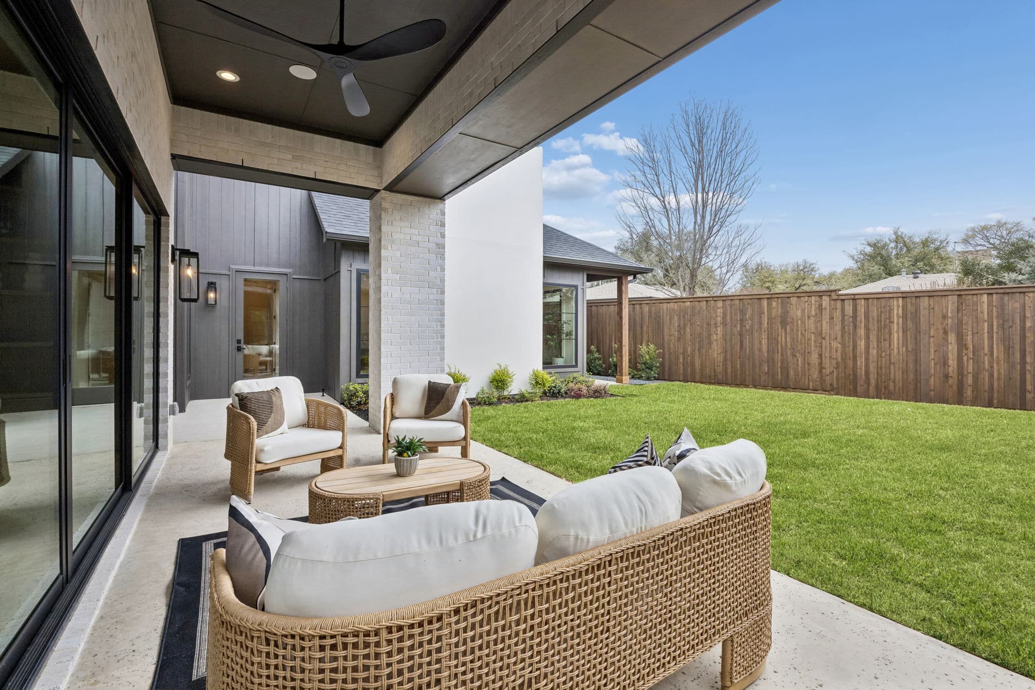 The covered patio at 7272 Tangleglen, woven seating under a dark ceiling looking out across the lawn.