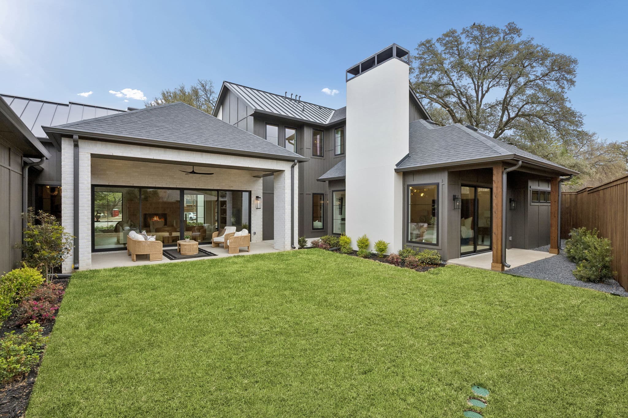 The back of 7272 Tangleglen, a covered porch beside a white chimney with lawn running the width of the garden.