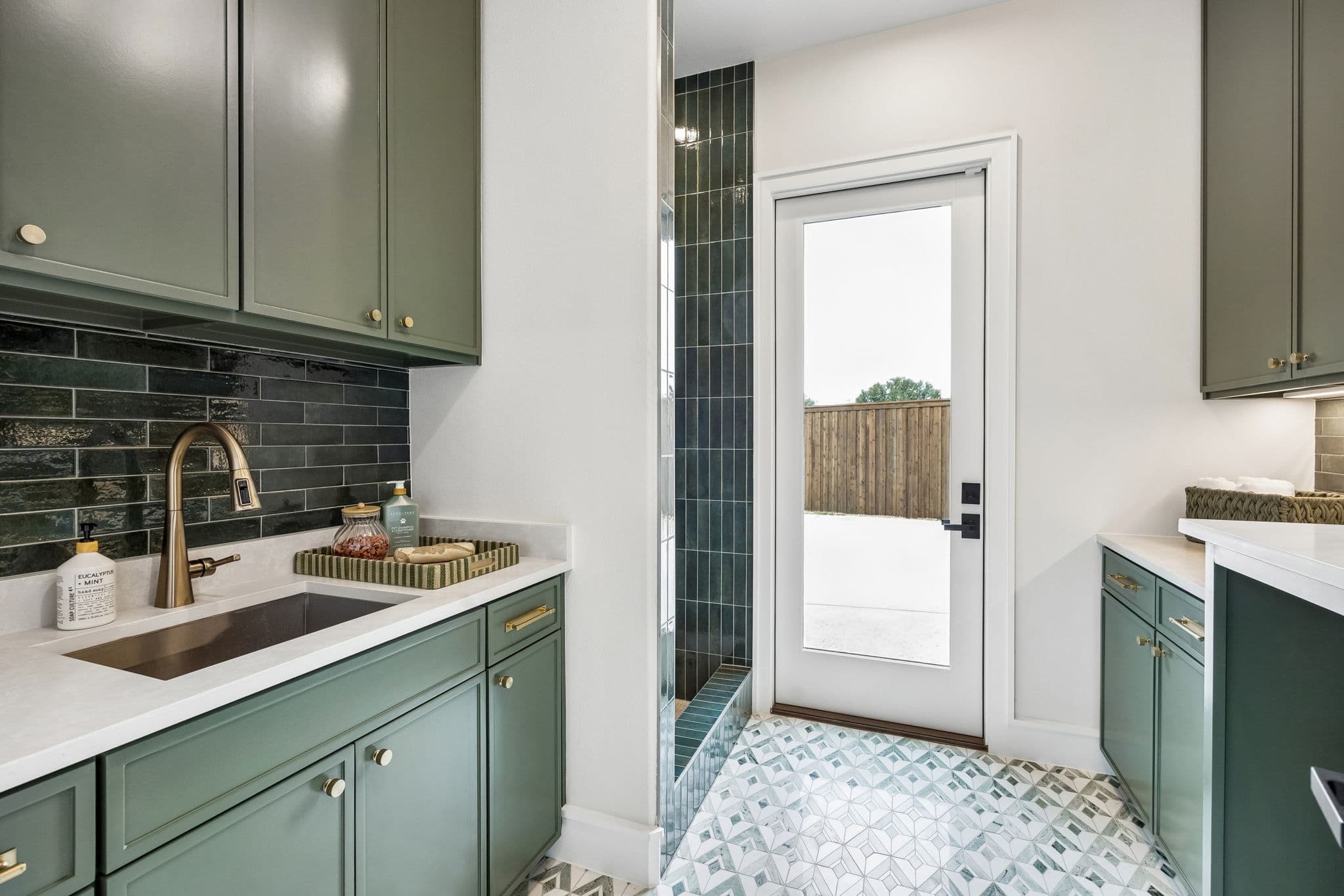 The bar at 7272 Tangleglen, deep green cabinetry under a brass tap and sink, with a glazed door to the side garden.