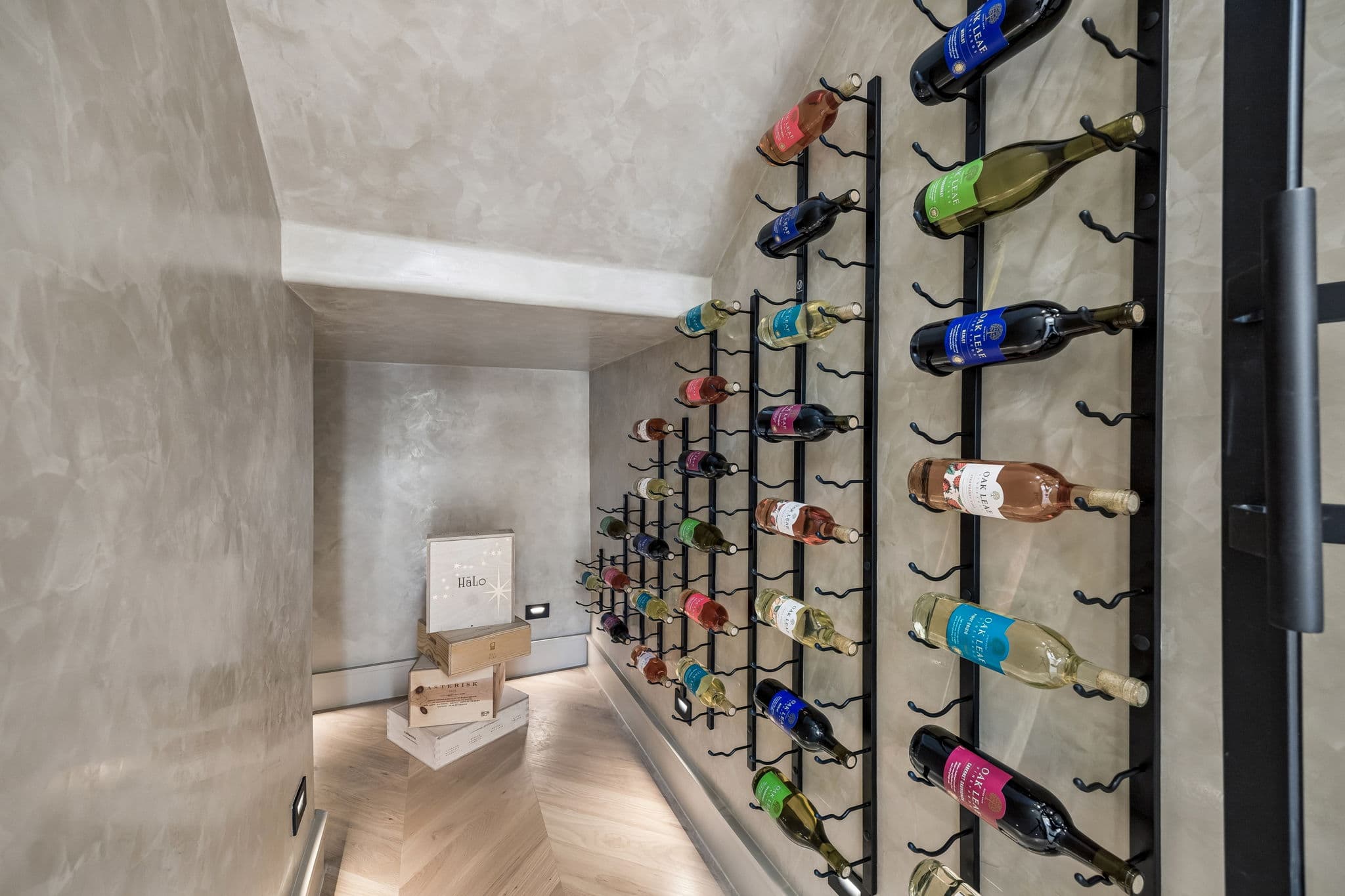 The wine wall at 7272 Tangleglen, bottles racked in rows against plaster beside the chimney.