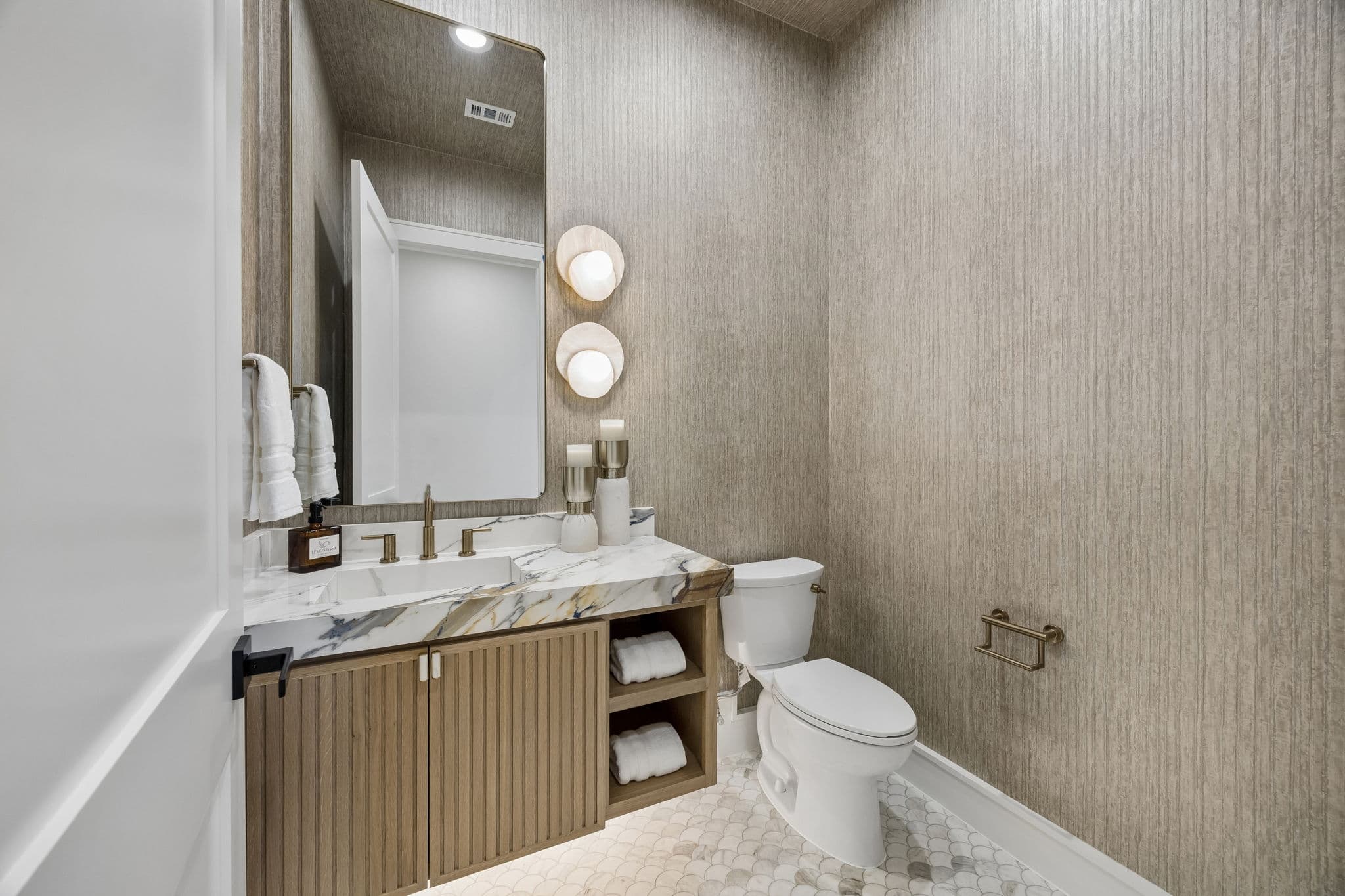 The powder room at 7272 Tangleglen, a grasscloth wall above a wood vanity with a slim mirror over it.
