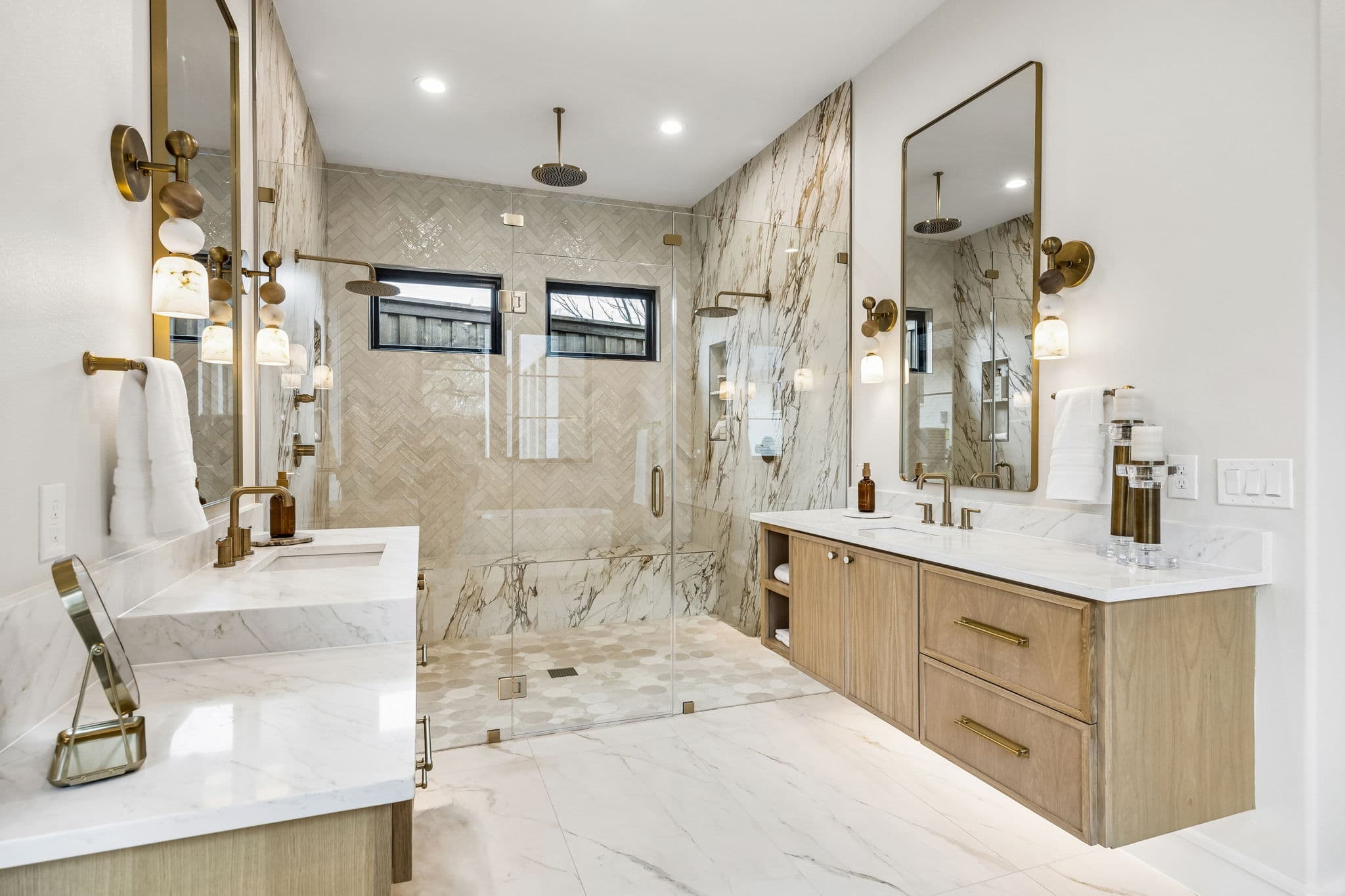 The primary vanity at 7272 Tangleglen, twin basins under brass sconces with mirrors on the marble wall behind.