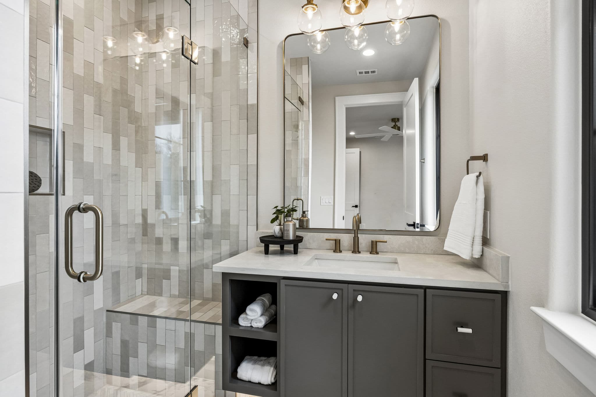 A guest bath at 7272 Tangleglen, a glazed shower beside a stone vanity under a round mirror.