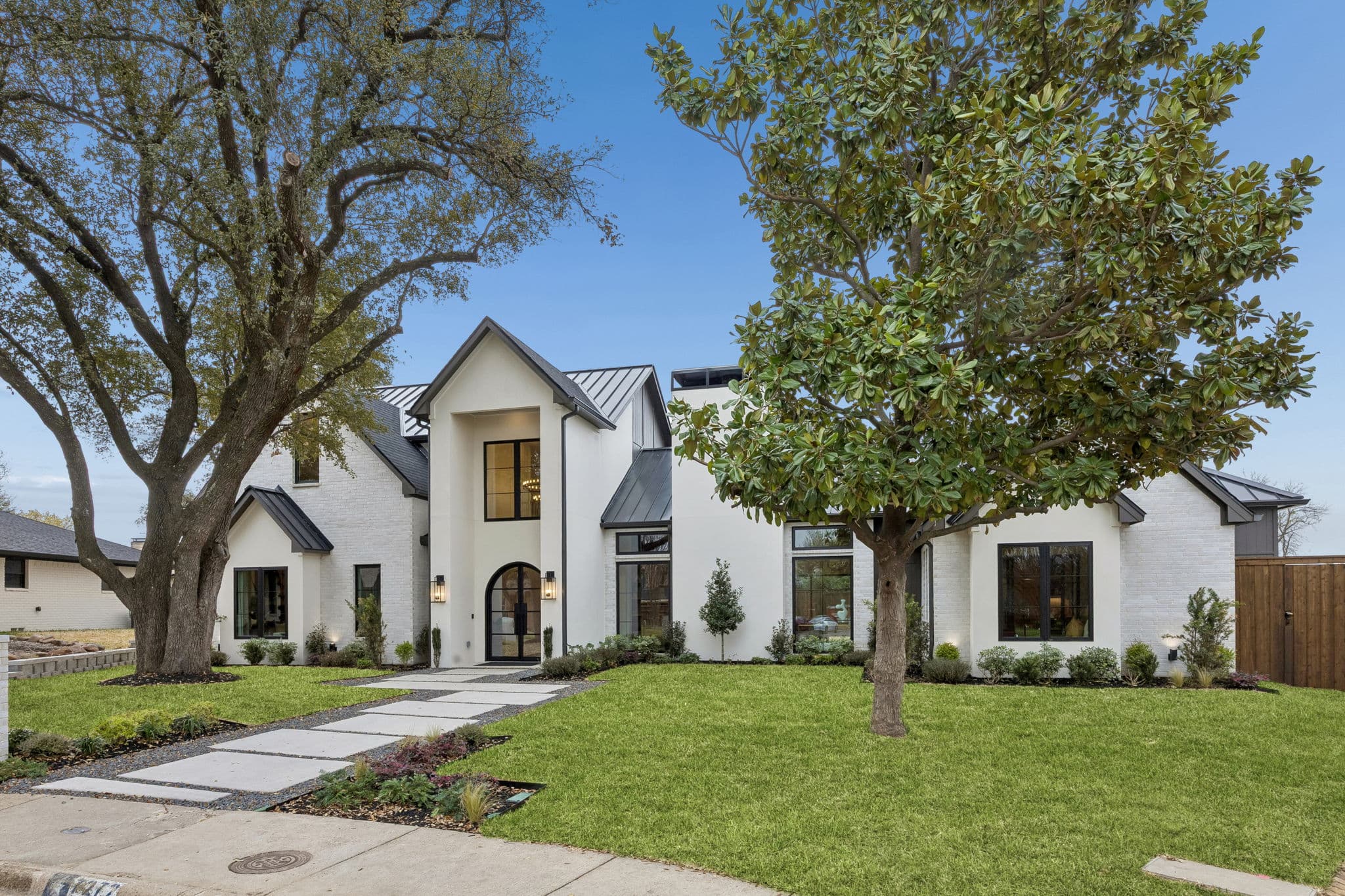 The front of 7272 Tangleglen, a white house with a standing seam roof behind two mature oaks.