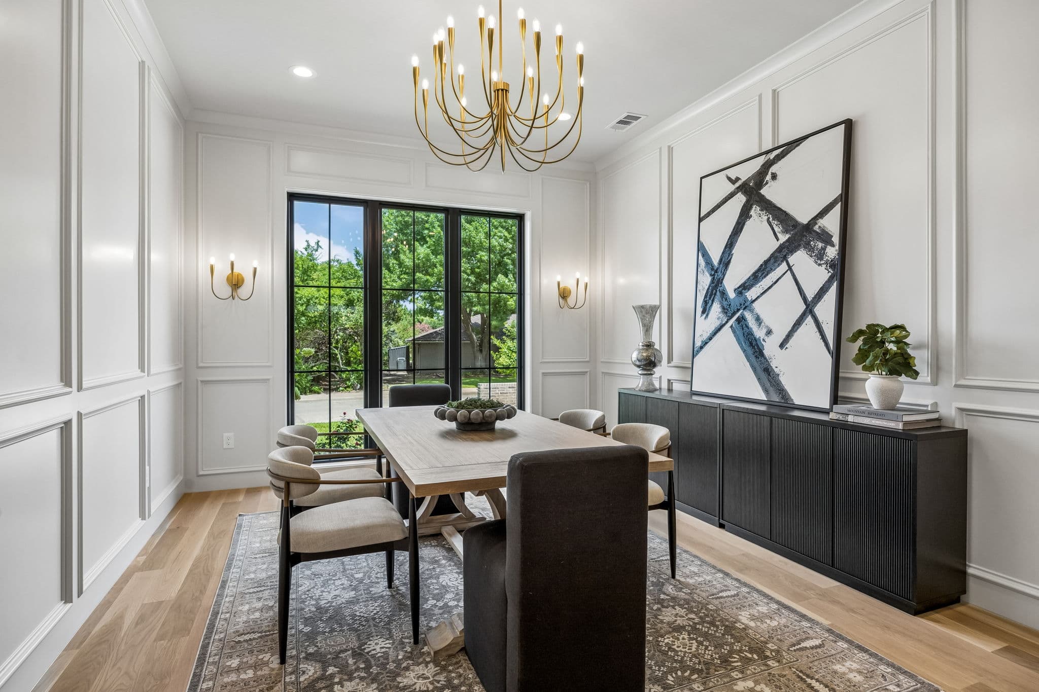 The dining room at 7308 Tangleglen, a brass chandelier over a light oak table with panelled walls and a tall steel window.