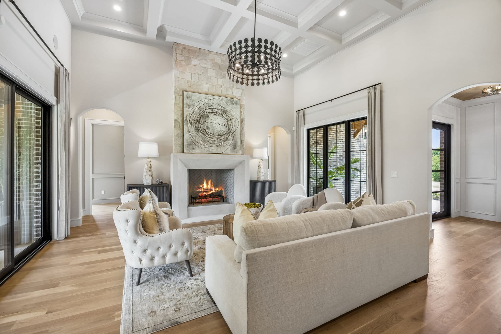 The living room at 7308 Tangleglen, a lit fireplace in a pale stone surround under a coffered ceiling with steel windows down both sides.