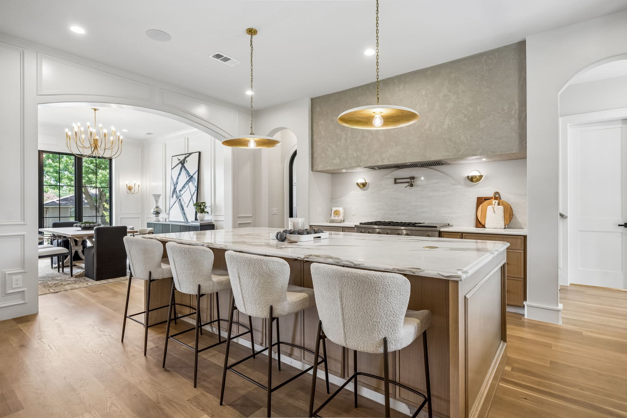 The kitchen at 7308 Tangleglen, a marble island with stools under two brass pendants and a plaster hood behind.