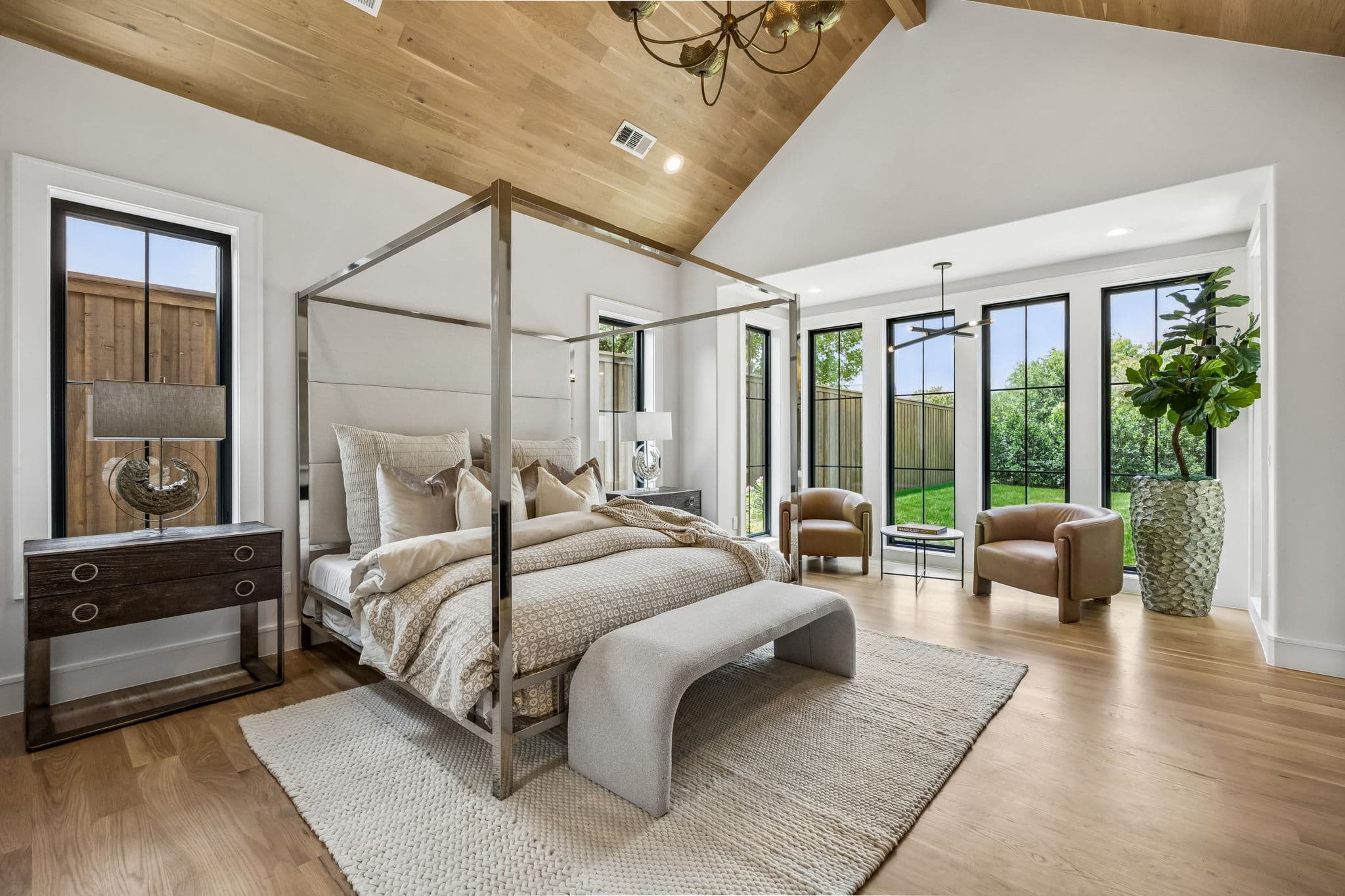 The primary bedroom at 7308 Tangleglen, a four poster bed under a vaulted oak ceiling with windows along two walls.