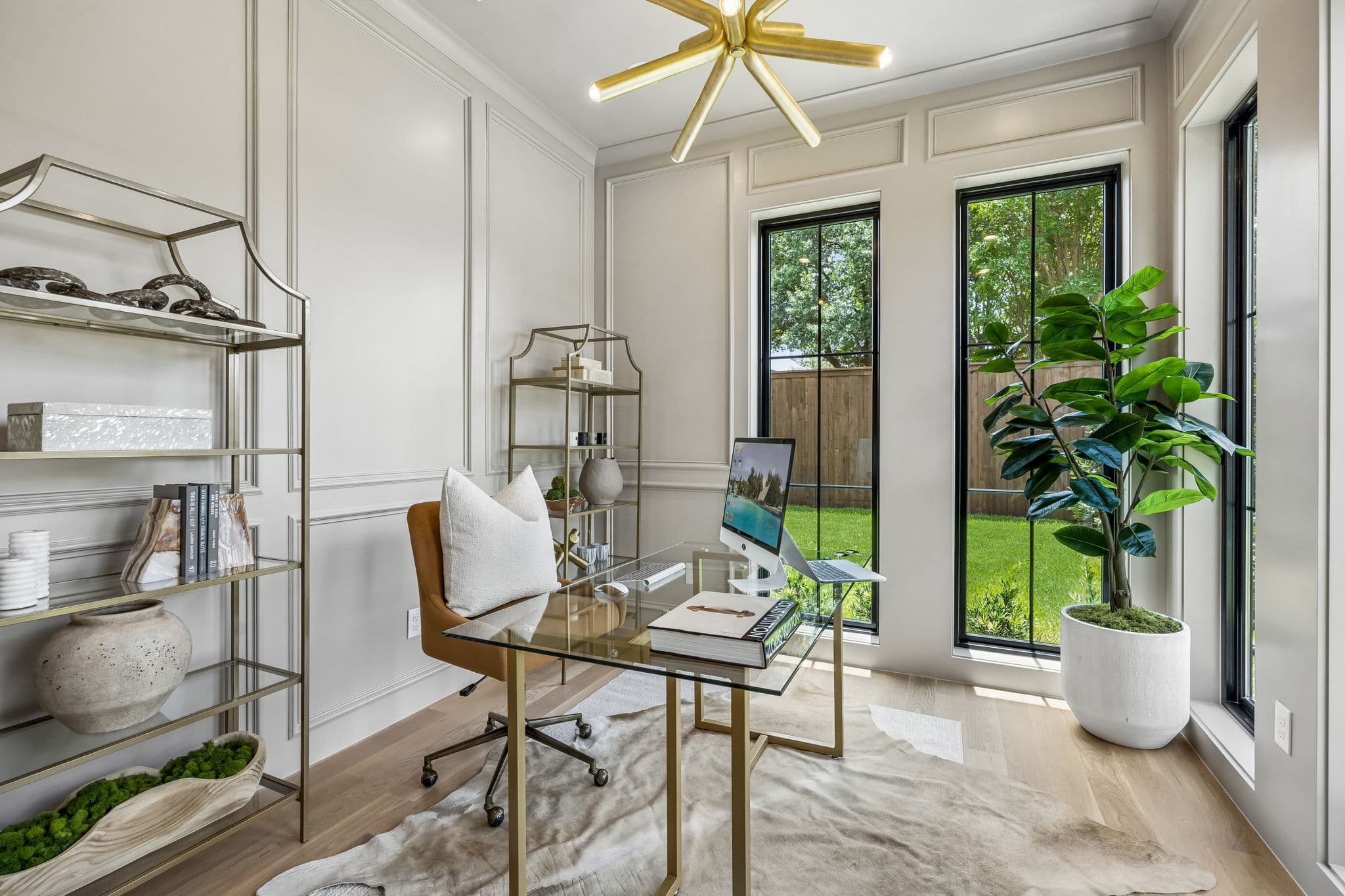 The study at 7308 Tangleglen, a glass desk between tall windows with plants along the sill.