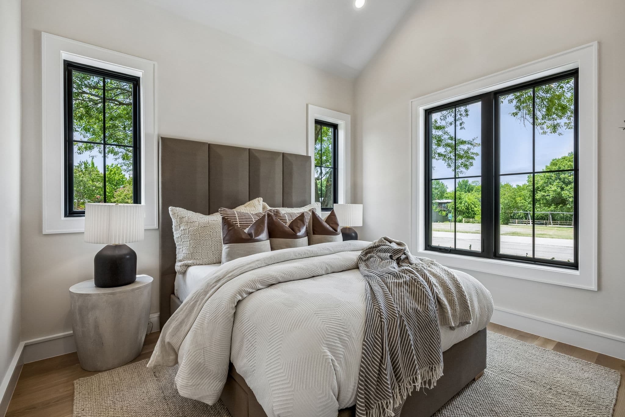 A bedroom at 7308 Tangleglen, an upholstered headboard between two windows under a vaulted ceiling.