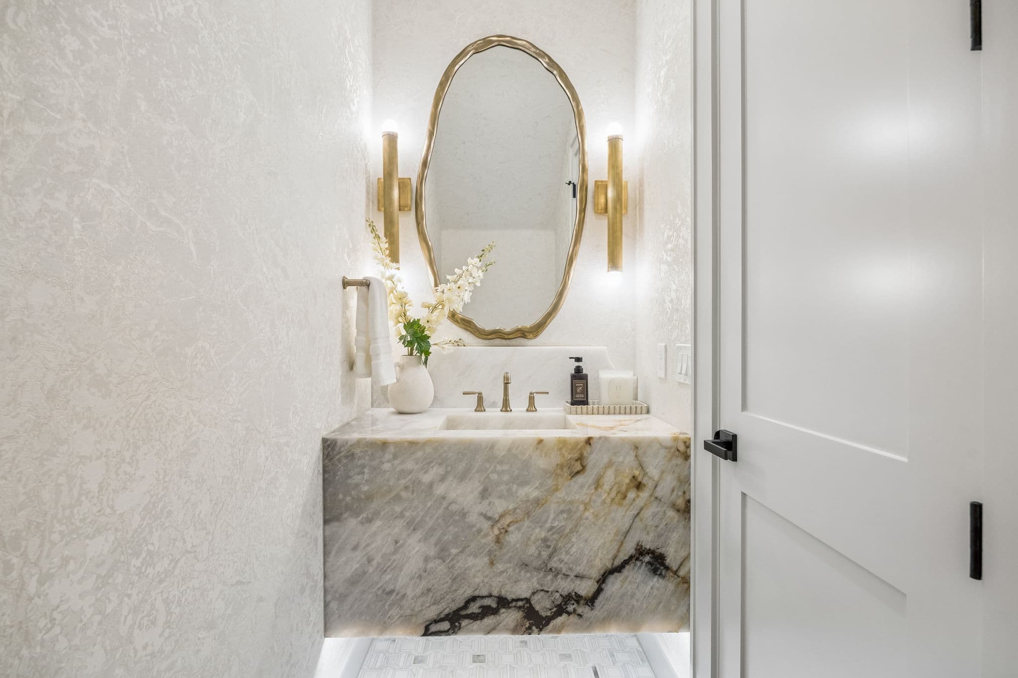 The powder room at 7308 Tangleglen, a marble counter under an arched mirror with a brass sconce beside it.