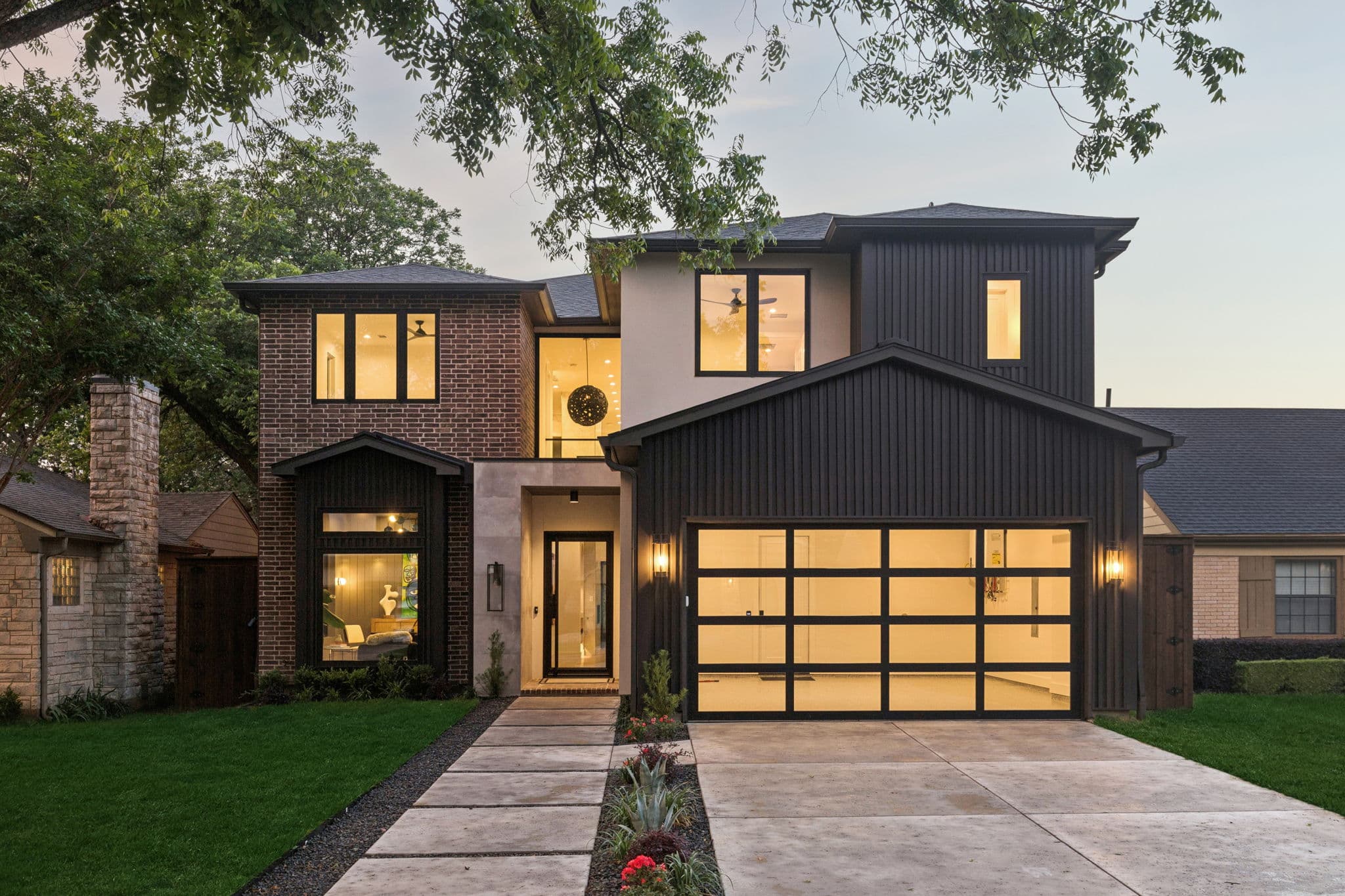 The front of 7615 Morton at dusk, brick and dark board under a lit glass garage door.
