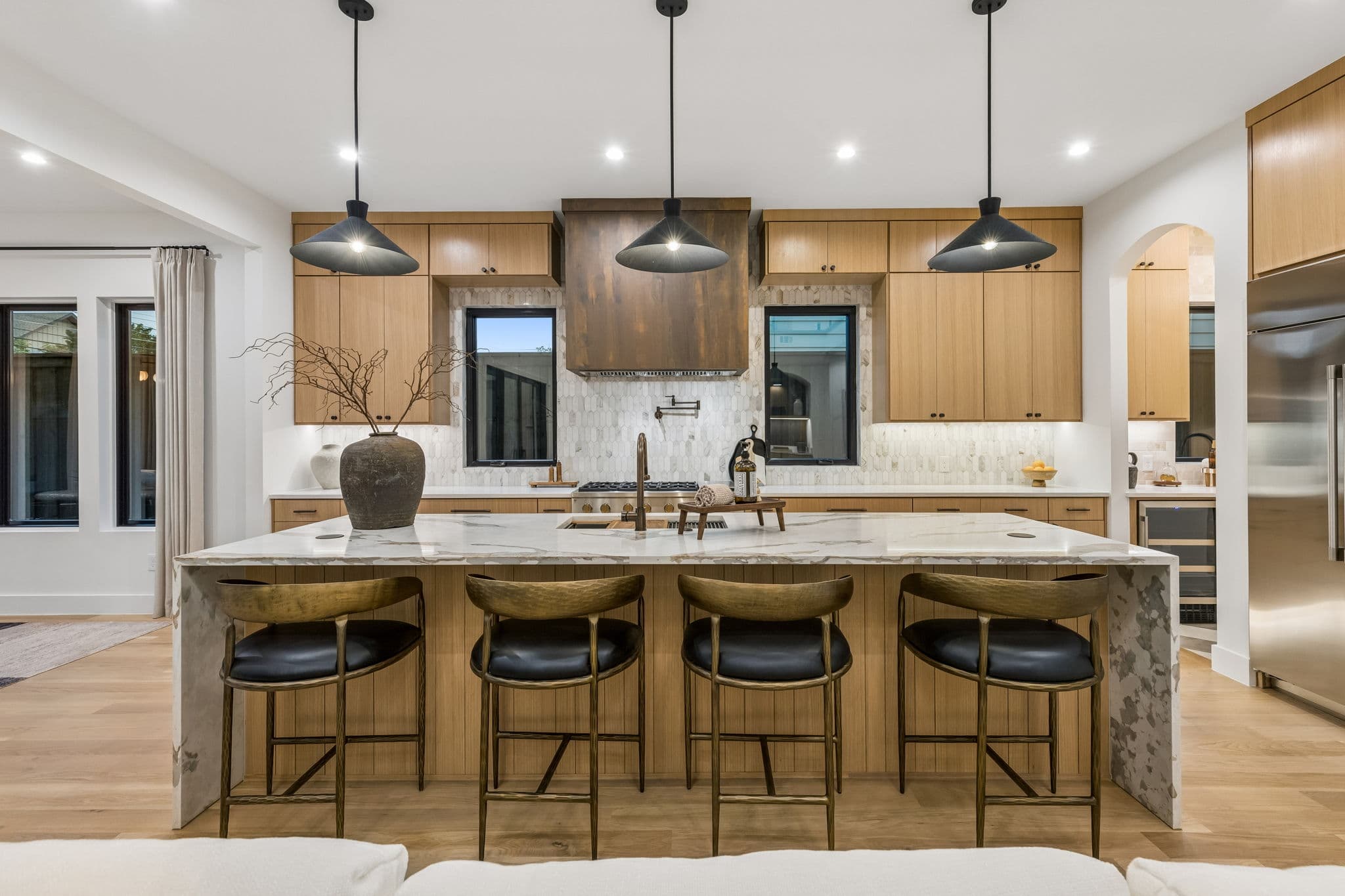 Kitchen at 7615 Morton, a long island in pale oak under three black pendants.