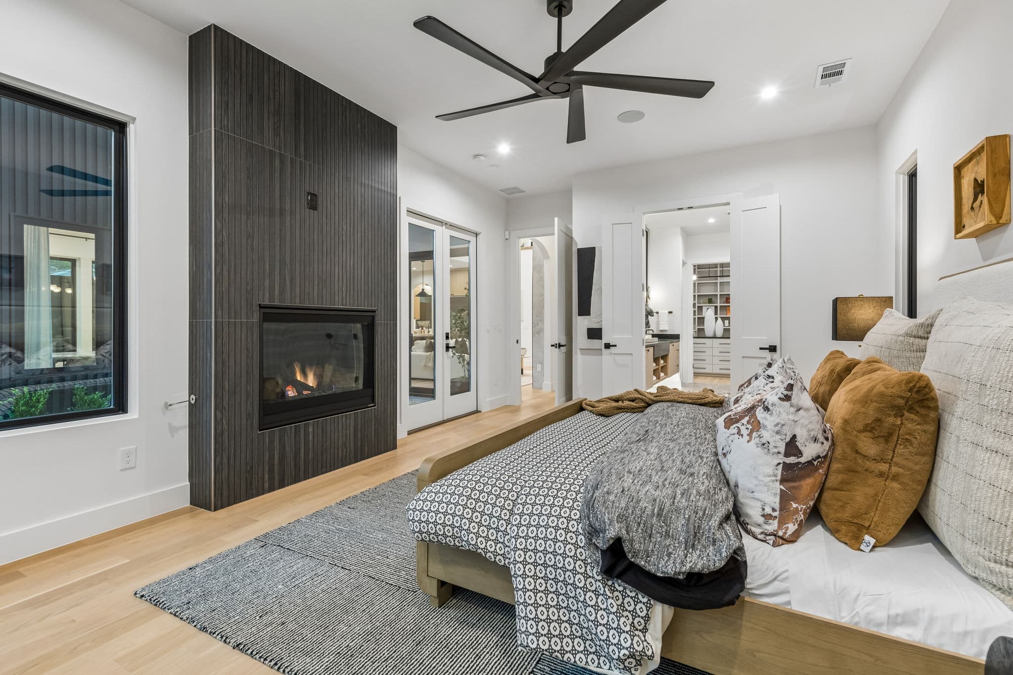 The primary bedroom at 7615 Morton, a dark timber wall carrying a fireplace with doors onto the garden.