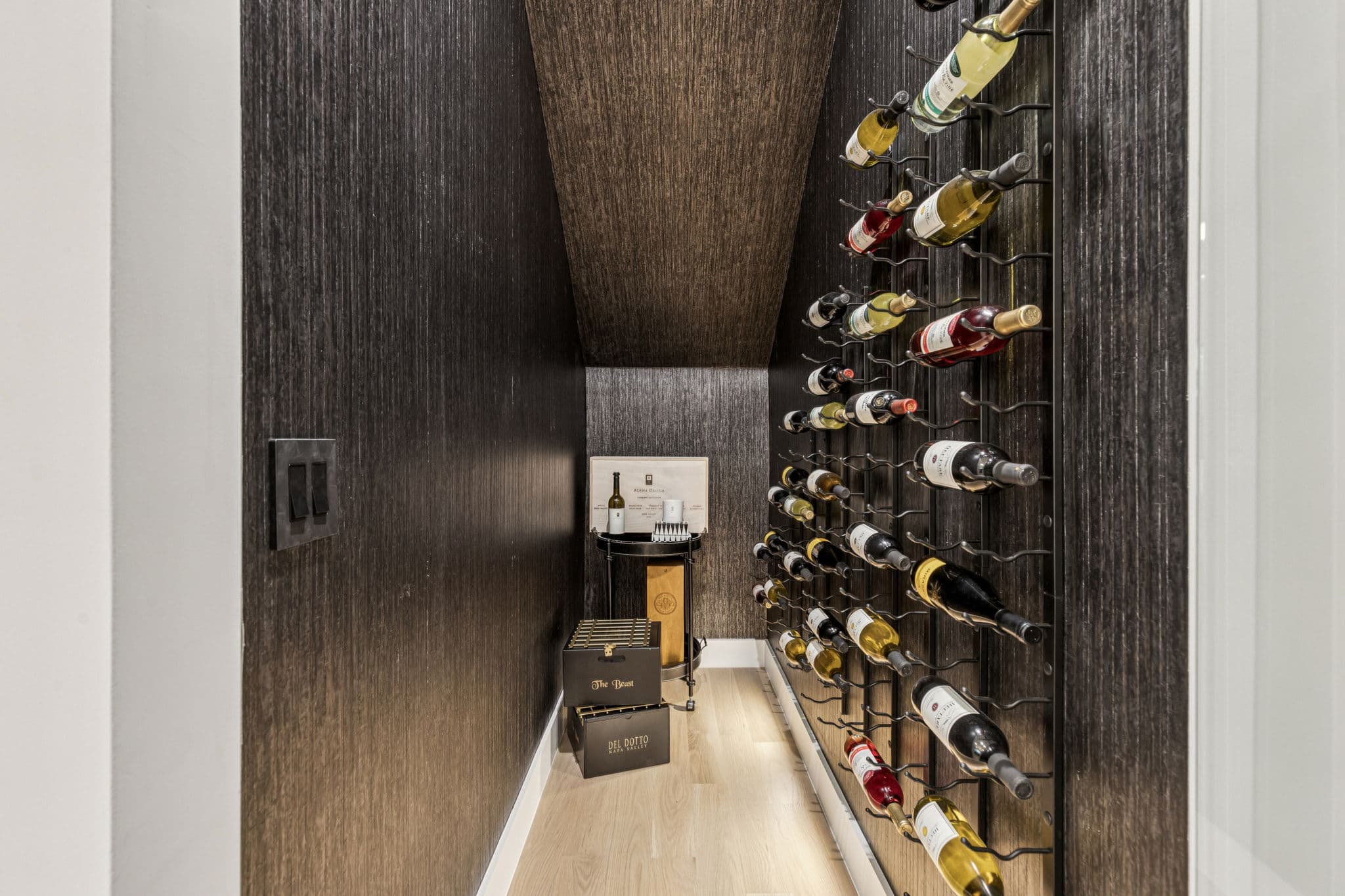 The wine room at 7707 Robin Road, bottles racked against dark timber in a narrow lit room.