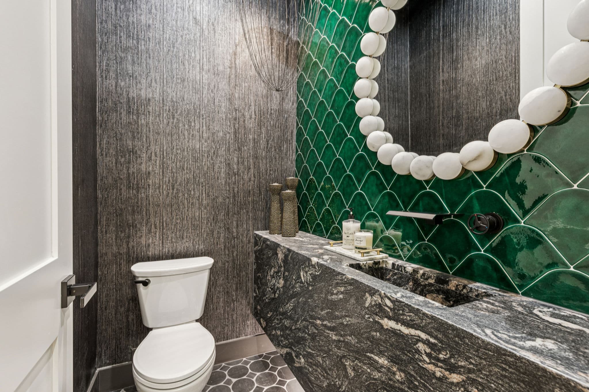 A powder room at 7707 Robin Road, green glazed tile above a dark stone counter.
