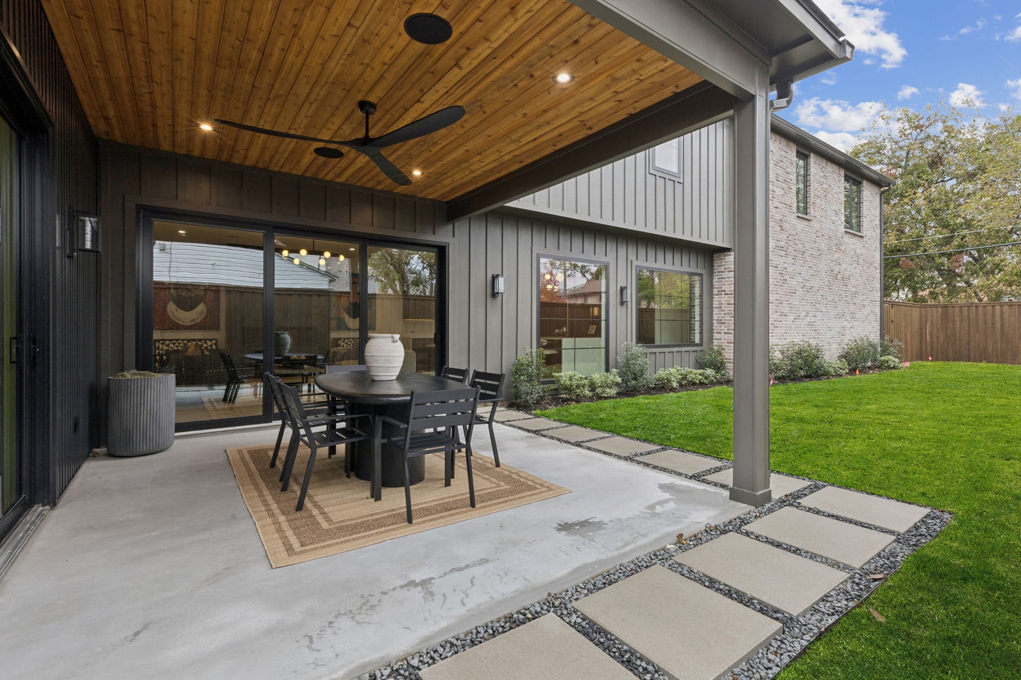 The covered patio at 7707 Robin Road, a wood ceiling over a dining table opening onto the lawn.