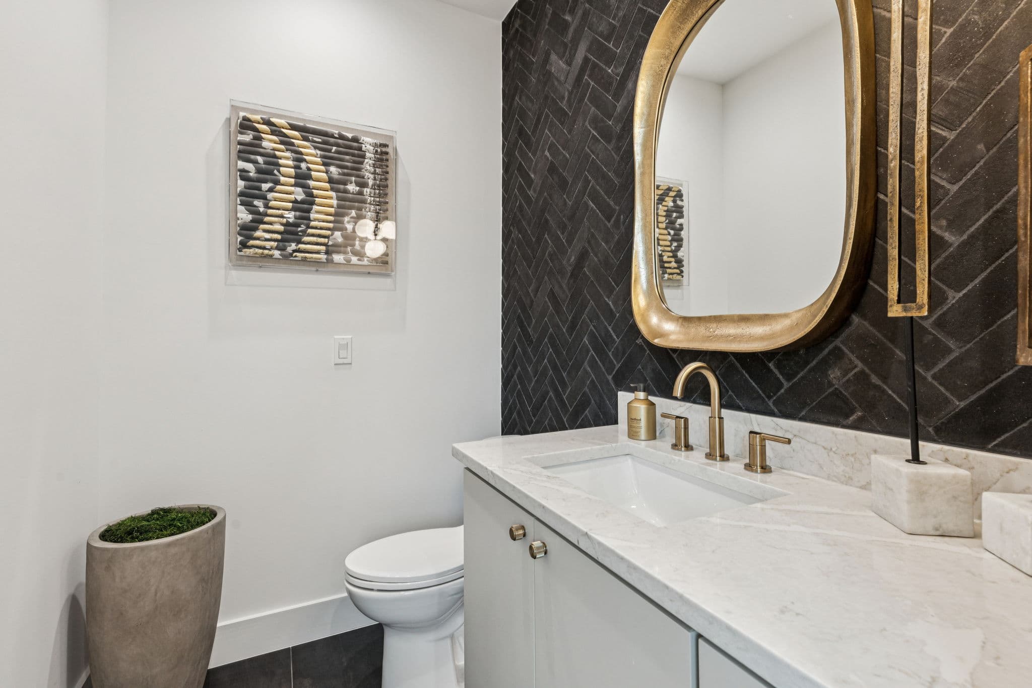The powder room at 7707 Robin Road, a gold mirror above a stone counter against dark tile.