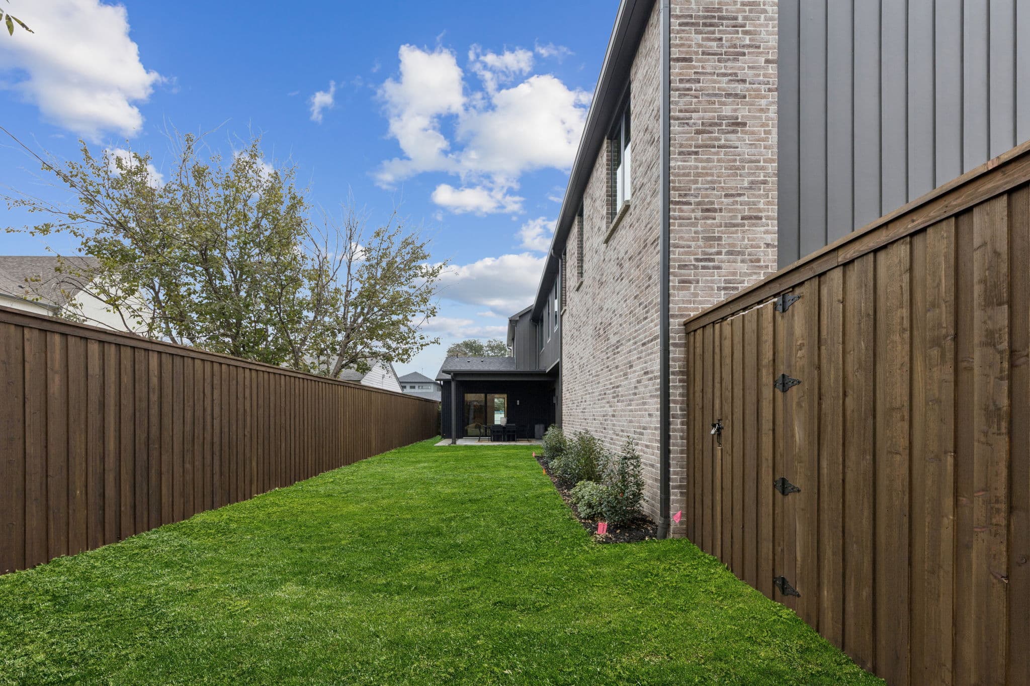 The back of 7707 Robin Road, brick and dark siding above a lawn enclosed by a timber fence.
